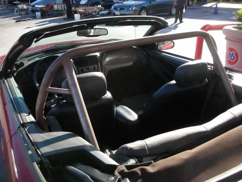 1998 Ford Crown Victoria - interior of a red convertible with the top down shows a welded roll bar and black leather seats in a parking lot.