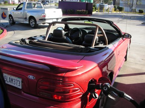 1998 Ford Crown Victoria - red Ford Mustang convertible with a roll bar refuels at a gas station, a white Ford pickup behind it; plate 5LAM373.