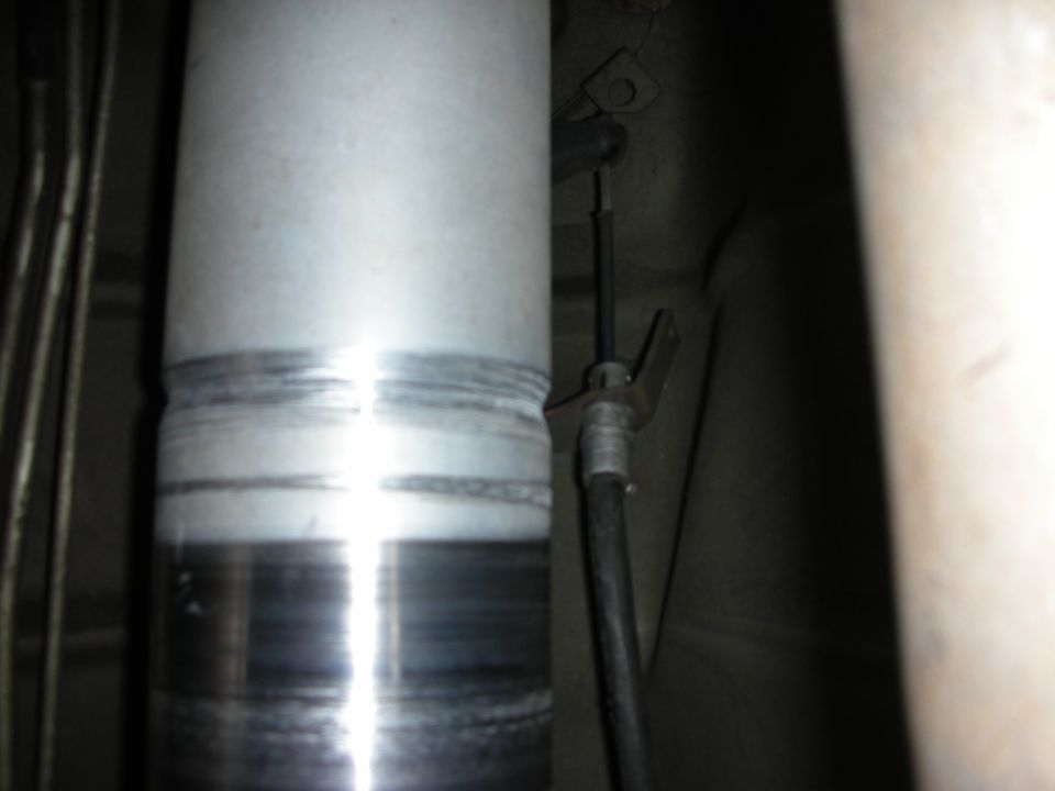 Underbody close-up of a polished aluminum driveshaft and brake cable bracket