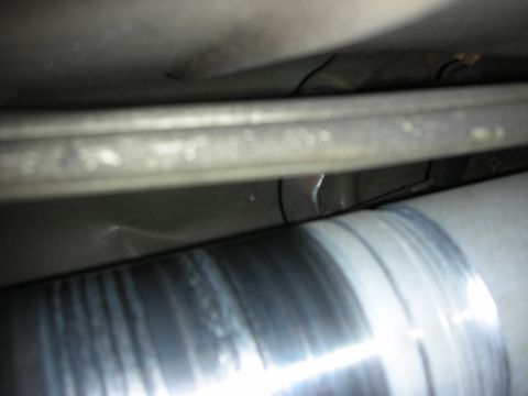 1998 Ford Crown Victoria - dark underbody close-up showing a polished metal driveshaft running beside a chassis frame rail.