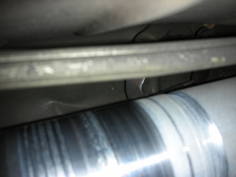 Dark underbody close-up of a polished driveshaft and chassis frame rail