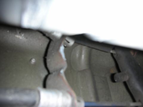1998 Ford Crown Victoria - blurry underbody close-up of a welded mounting bracket and surrounding chassis components beneath a vehicle.