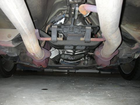 1998 Ford Crown Victoria - View from beneath a vehicle showing the transmission mount crossmember flanked by dual exhaust pipes and the rear suspension.