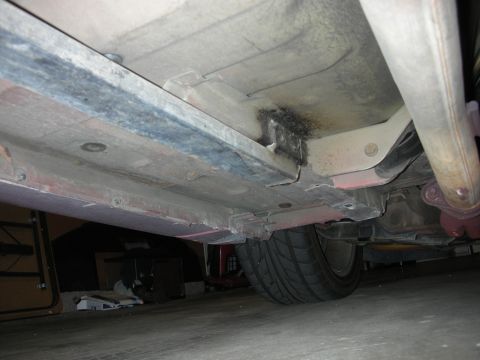 1998 Ford Crown Victoria - Underbody shot of a car's floor pan and frame rail with welds and a rear tire, taken on a garage floor.