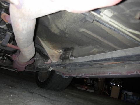 1998 Ford Crown Victoria - Underbody view of a car's frame rail and exhaust pipe near the rear wheel, photographed in a workshop.