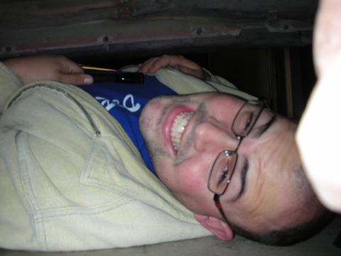 1998 Ford Crown Victoria - smiling man in glasses and a hooded jacket lies on his back working under a vehicle.