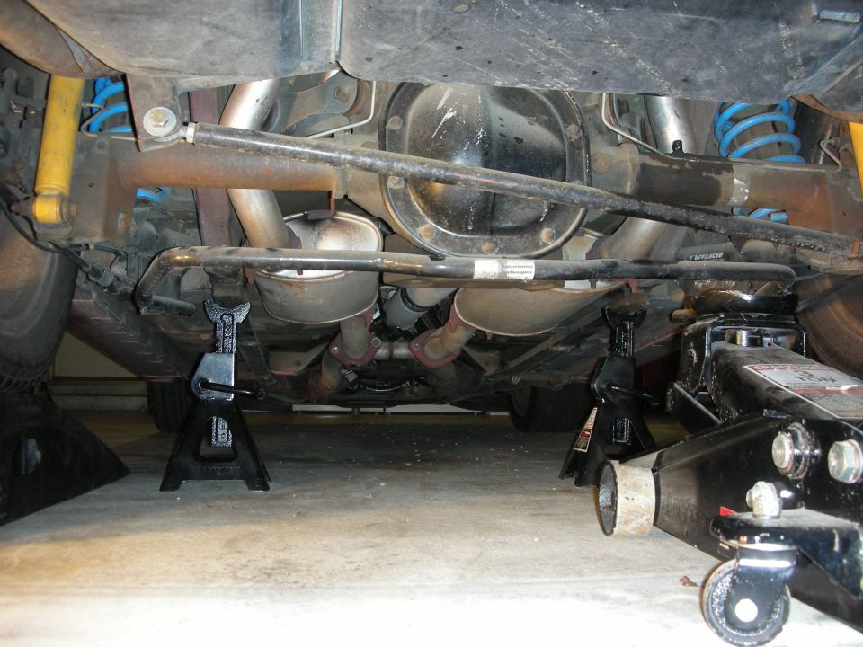 Rear underside of a car on jack stands showing exhaust, rear axle and coil springs