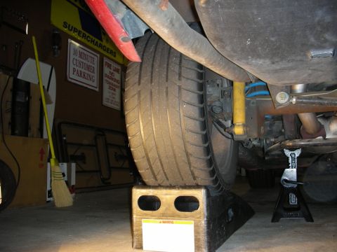 1998 Ford Crown Victoria - car's rear tire sits on a wheel ramp block in a garage, with a jack stand and a 'Superchargers' sign nearby.