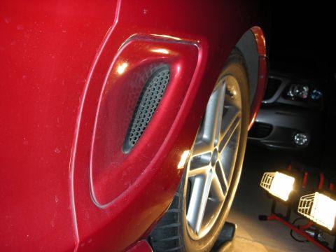 1998 Ford Crown Victoria - Night close-up of a red car's rear quarter-panel mesh air scoop above a silver five-spoke alloy wheel.