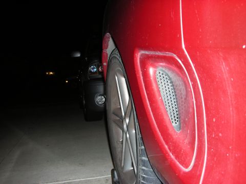 1998 Ford Crown Victoria - red car's rear quarter panel with a mesh vent scoop and five-spoke alloy wheel, photographed outdoors at night.