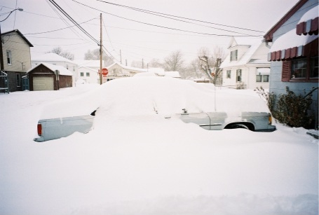 1989 Ford LTD Crown Victoria - Two cars buried nearly to the roofline in deep snow in a residential driveway, with only the light-colored trunk lids, rear quarter panels…