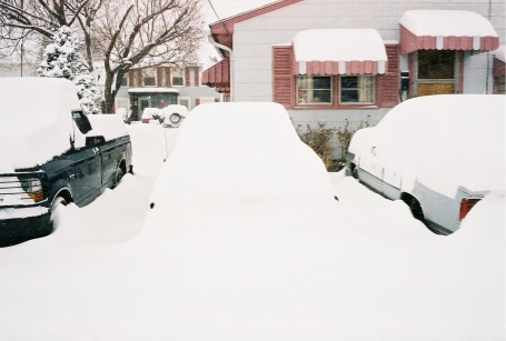 1989 Ford LTD Crown Victoria - Three vehicles buried under deep snow in a driveway after a heavy snowfall, a dark pickup with a snow-covered bed at left, a completely bla…