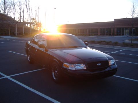 2001 Ford Crown Victoria - A black 2001 Ford Crown Victoria is parked in a lot as the sun sets, casting a warm glow.