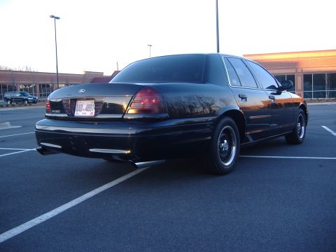 2001 Ford Crown Victoria - Rear view of a black 2001 Ford Crown Victoria parked in a lot, showing its distinctive taillights and dual exhaust.