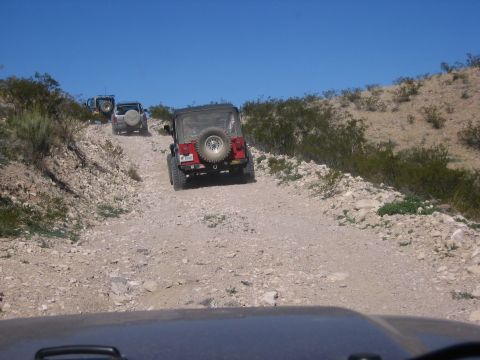 1996 Ford Bronco - Several Jeeps navigate a challenging dirt road in a dry, arid environment under a bright blue sky.