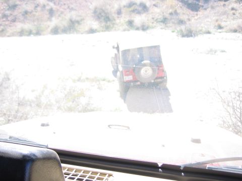1996 Ford Bronco - Two vehicles on a dirt road in a dry, hilly area. The rear of a red Jeep Wrangler is visible.