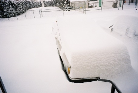 1989 Ford LTD Crown Victoria - A vehicle sits completely buried under deep fresh snow in a chain-link fenced yard, its outline barely readable with a small antenna flag p…
