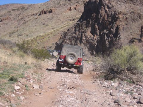 1996 Ford Bronco - Two Jeep Wranglers navigate a , rocky trail through a desert landscape under a clear blue sky.