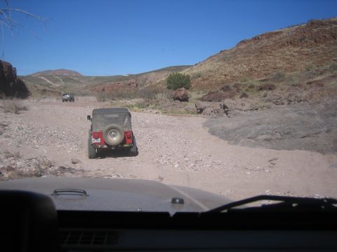 1996 Ford Bronco - Two Jeeps navigate a rough, rocky terrain under a clear blue sky.