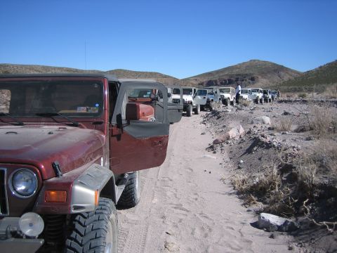 1996 Ford Bronco - Multiple Jeeps are lined up on a dusty trail with mountains in the background.