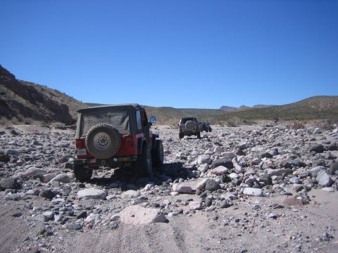 1996 Ford Bronco - Several off-road vehicles navigate a , rocky terrain on a sunny day.