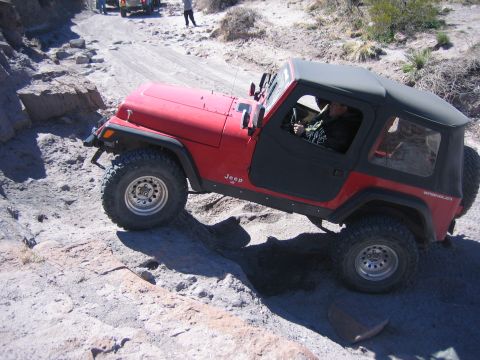 1996 Ford Bronco - A red Jeep Wrangler navigates a challenging rocky terrain with another vehicle visible in the background.