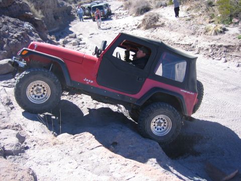 1996 Ford Bronco - A red Jeep Wrangler navigates a rocky trail, with other off-road vehicles visible in the distance.