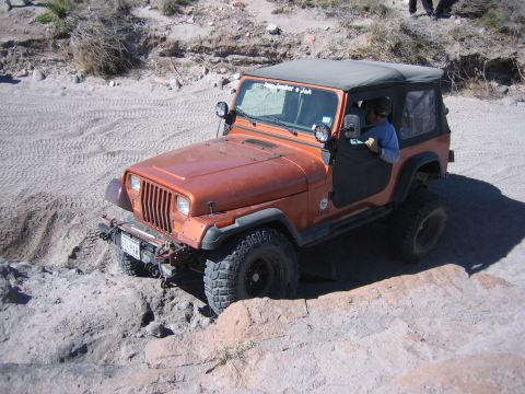 1996 Ford Bronco - A driver navigates an off-road trail in an orange Jeep Wrangler with the door open.