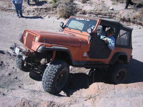1996 Ford Bronco - An orange Jeep Wrangler navigates a rocky, off-road course with a driver inside.