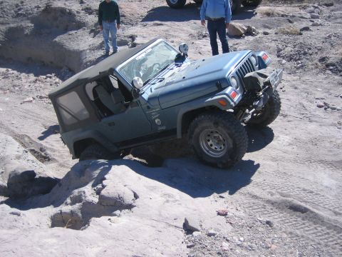1996 Ford Bronco - A Jeep Wrangler TJ is shown off-roading on a rocky, sandy trail with two onlookers.
