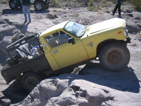 1996 Ford Bronco - A yellow Toyota pickup truck navigates a rocky off-road course, with another vehicle visible in the background.