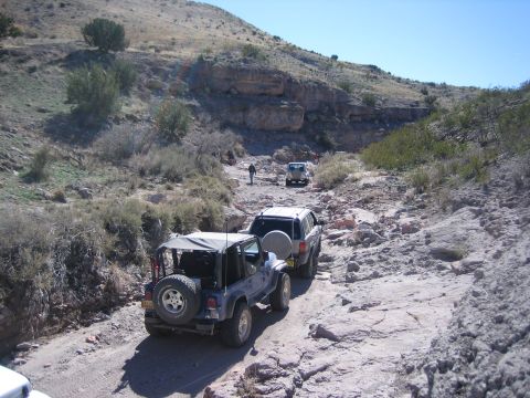 1996 Ford Bronco - Multiple off-road vehicles traverse a challenging rocky trail in a desert landscape.