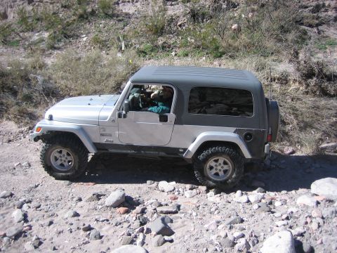 1996 Ford Bronco - A driver navigates a Jeep Wrangler over a rough, rocky terrain with sparse vegetation.