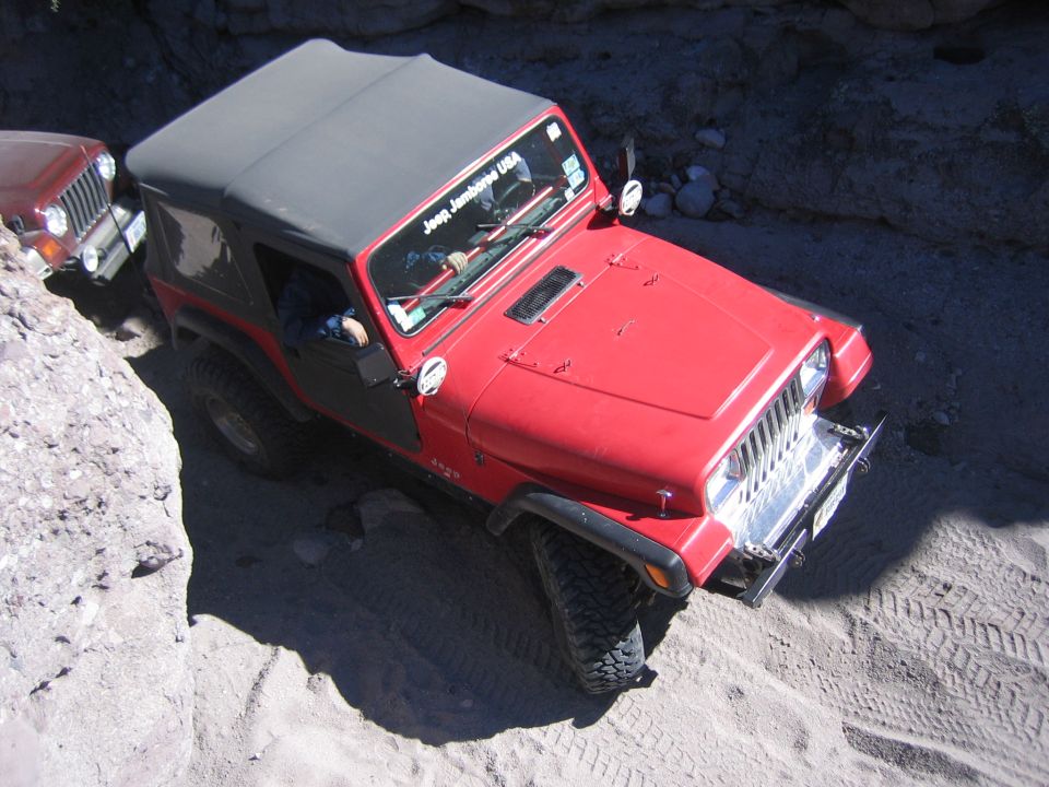 Red Jeep Wrangler with a grey soft top, driving on a sandy trail