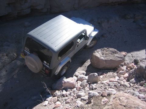 1996 Ford Bronco - Jeep Wrangler TJ off-roading on a rocky trail, with a spare tire mounted on the back.