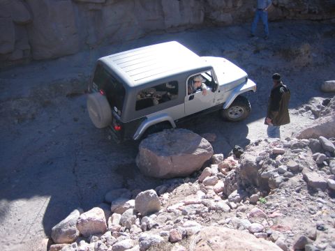 1996 Ford Bronco - A Jeep Wrangler TJ maneuvers through a challenging, rocky off-road path with a driver at the wheel.