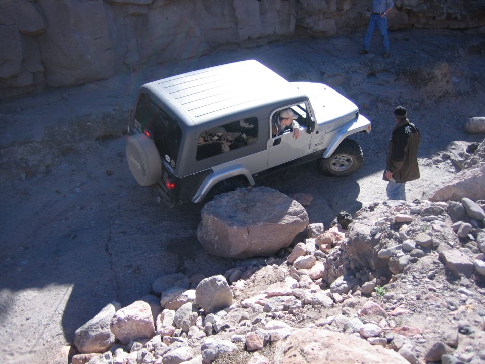 Silver Jeep Wrangler TJ navigating rocky terrain, driver visible