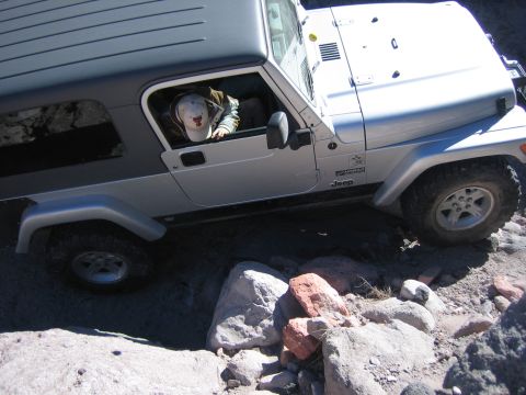 1996 Ford Bronco - A silver Jeep Wrangler is shown maneuvering through a challenging rocky path, with the driver looking out the window.