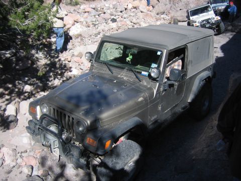 1996 Ford Bronco - A Jeep Wrangler navigates a challenging rocky terrain with other vehicles visible in the background.