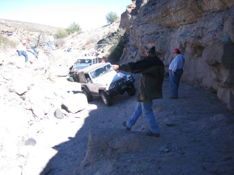 1996 Ford Bronco - Several Jeep Wranglers traverse a narrow, rocky canyon path with onlookers observing the off-road adventure.