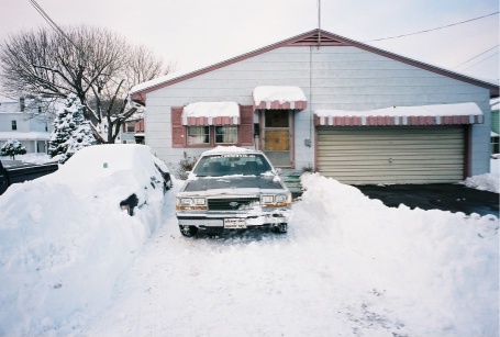 1989 Ford LTD Crown Victoria - A boxy 1980s Ford Crown Victoria sedan dug out of deep snow in front of a single-story house, viewed head-on between tall shoveled snowbank…