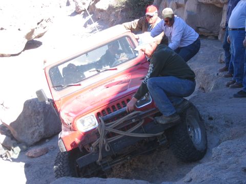 1996 Ford Bronco - A red Jeep Wrangler is being helped by several people as it navigates a challenging rocky terrain.