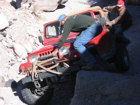 1996 Ford Bronco - Two people attempt to free a red Jeep Wrangler that is stuck on a rocky trail.