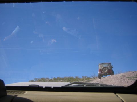 1996 Ford Bronco - A red Jeep Wrangler is seen from inside another vehicle, driving up a dusty hill.