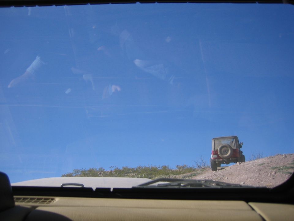 Jeep Wrangler driving up a dirt hill under a clear blue sky