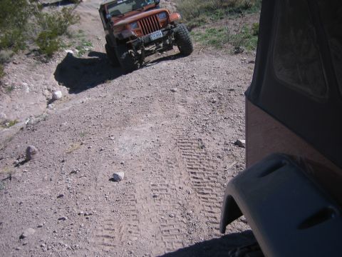 1996 Ford Bronco - An orange Jeep Wrangler navigates a dirt path, with another vehicle partially visible in the foreground.