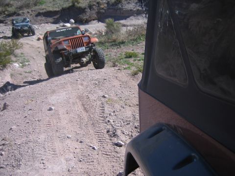 1996 Ford Bronco - Two Jeeps navigate a dusty trail, with the lead vehicle in an orange hue and the second vehicle further up the path.