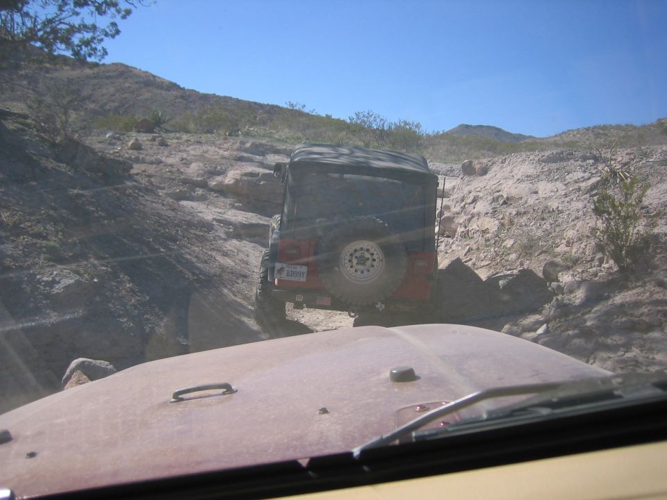 Red Jeep Wrangler with spare tire on rear, driving on rocky terrain