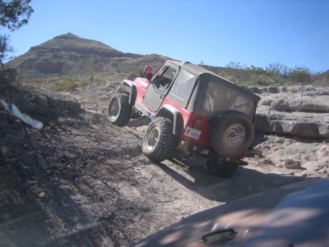 1996 Ford Bronco - A red Jeep Wrangler navigates a steep, rocky trail under a clear blue sky.