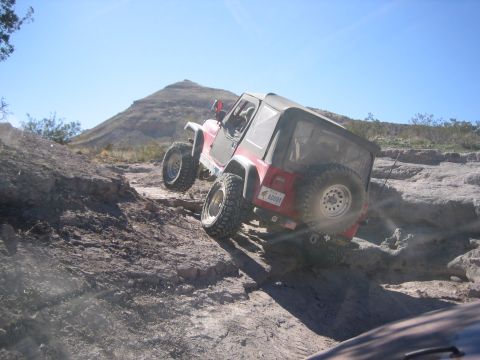 1996 Ford Bronco - Jeep Wrangler tackling a challenging off-road trail under a clear blue sky.